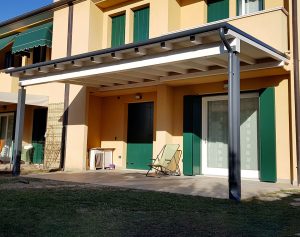 Tettoia in legno bianca con colonne in metallo addossata alla parete di una casa a Treviso