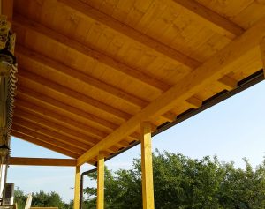 Tettoia in legno addossata a parete con tavole e travi verniciati